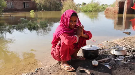 Woman kneeling in front of kitchen utensils in flooded area in Pakistan