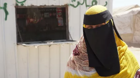 Yemen_Woman in black and yellow burqa standing in front of container