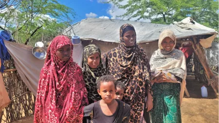Kenya_Woman in leopard print hijab standing with her 5 children outside stick house