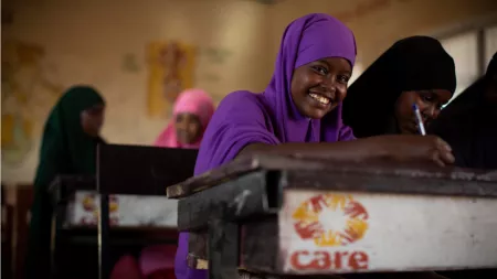 Somalia_Girl in purpule hijab sitting at CARE branded desk smiling at camera