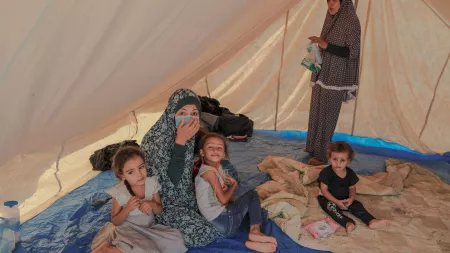 Woman with surgical mask sitting on the floor of a tent with three children