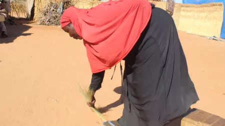 Woman in red and black sweeping dirt floor