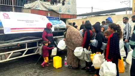 Line of people holding plastic large bottles in front of metal water truck