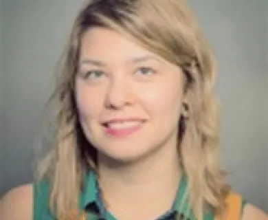 Headshot of woman smiling to the camera, with short straight blonde hair. Wearing green sleeveless shirt