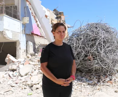 Turkiye_Woman in black shirt standing in front of destroyed building and ball of barbed wire