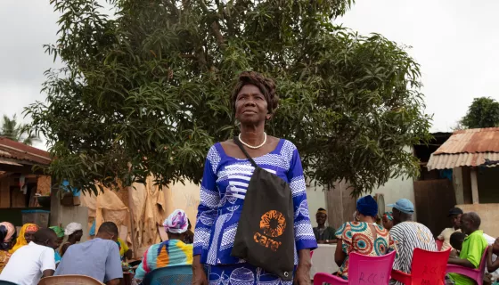 Woman standing up wearing blue and white dress and a bag with CARE's orange logo
