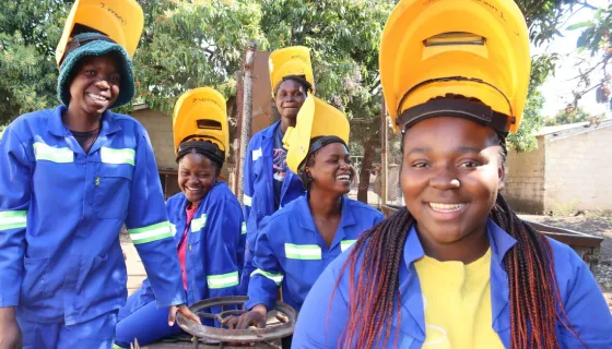 Group of girls smiling wearing blue jumpsuits and yellow shielding masks