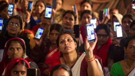 A group of Indian women sit together and hold up smartphones displaying an app.