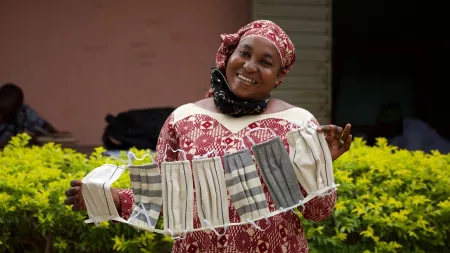 A woman smiles broadly while displaying the blue and white cloth face masks she has made.