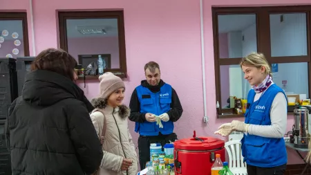 Two workers with CARE partner PAH provide food and water to Ukrainian refugees entering the Poland border.