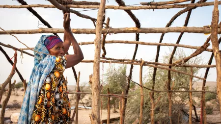 A woman looks over her shoulder while tying two pieces of wood together with rope.