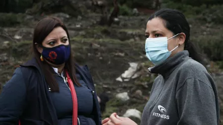 Two women wearing face masks stand and talk with each other.