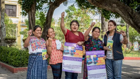 A group of five women raise their fists and hold signs advocating for dignified working conditions in Guatemala.