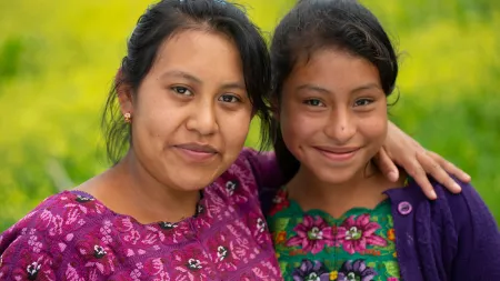 Two Guatemalan women stand together with their arms around each other's shoulders.