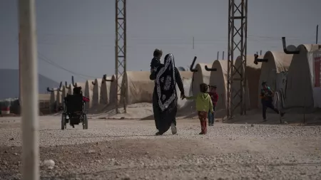 Woman walks in IDP camp with two children
