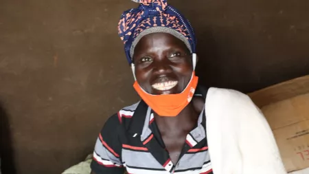 A woman smiles. She has an orange face mask pulled down so that her smile is visible.