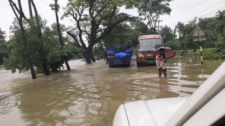 People and cars walk through flooded area in Bangladesh