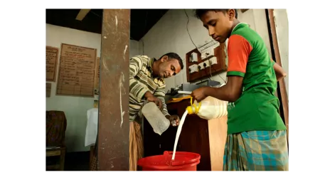 Bangladesh_man and boy pouring milk into red container