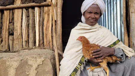 Woman holding chicken sitting in the floor in front of her house