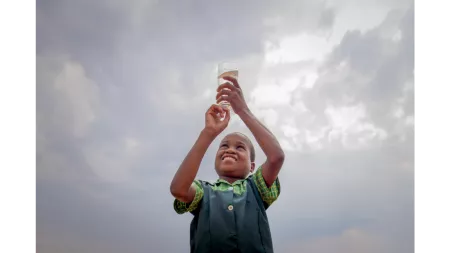 Zimbabwean child with green tunic holding a glass of water up