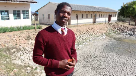 Zimbabwean boy in red uniform in front of classrooms