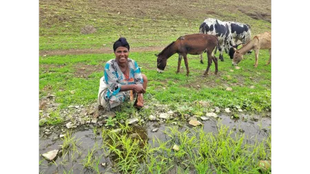 Ethiopia_Lady kneeling next to water source with livestock grazing behind her