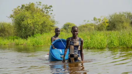 Two young women carry blue drum through a flooded area in South Sudan