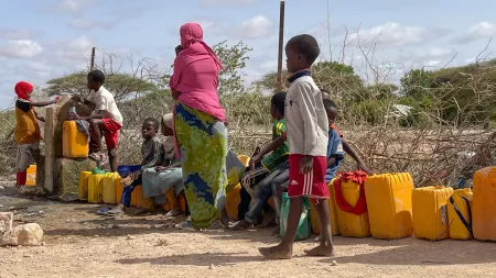 Children and a woman in front of water gallons in dry area