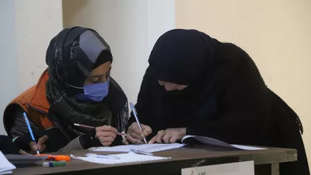 Woman signing document in front of other woman sitting down