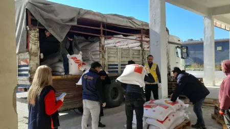 People carrying large flour bags out of a truck