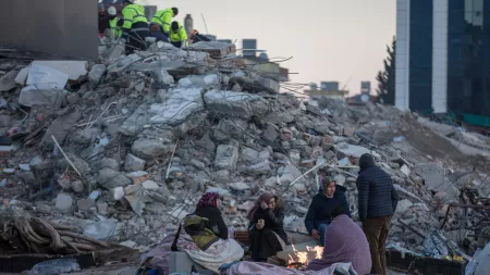 Women sitting around fire in front of rubble