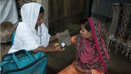 Bangladesh_Doctor sitting with woman on stoep checking blood pressure