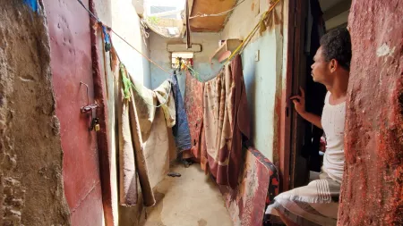 Yemen_Man standing at his doorway looking into alley where blankets are drying