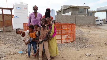 Yemen_Man standing with his wife and laughing children in front of circular orange cage