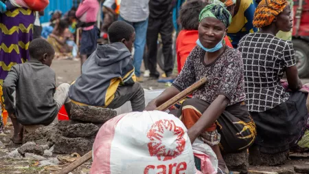 DRC_Woman sitting on a rock holding crutch with CARE aid package in front of her