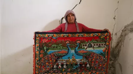 Syria_Woman standing with peacock tapestry in damaged home after earthquakes