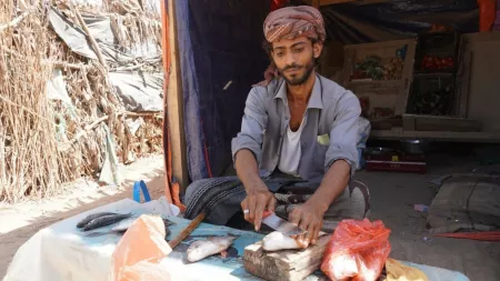 Yemen_Man gutting fish sitting on the floor in front of informal home