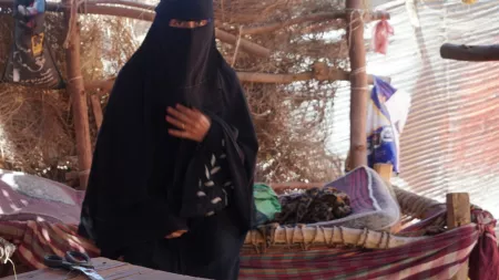 Yemen_Woman in full burqa standing under informal shelter with hamok bed