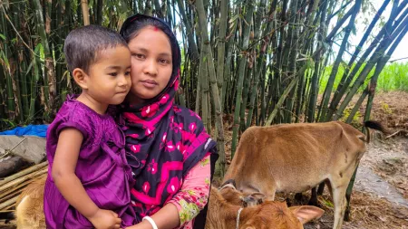 Bangladesh_Mother olding duaghter wearing purple dress in front of cows