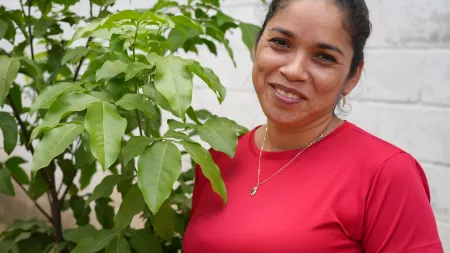 Honduras_Woman in red shirt standing by tree leaves smiling