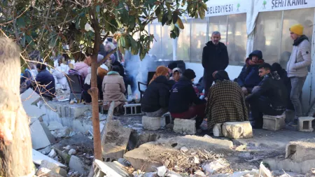 Turkiye-Syria_Groups of people sitting on bricks outside tent shelter