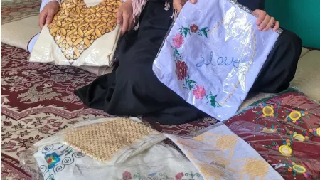 Afghanistan_Girls holding finished embroidered dresses in plastic packaging