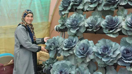 Jordan_Woman with spotted hijab smiling next to vertical cabbage garden