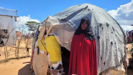 Kenya_Woman in red dress and black hijab standing in front on makeshift shelter at Dadaab