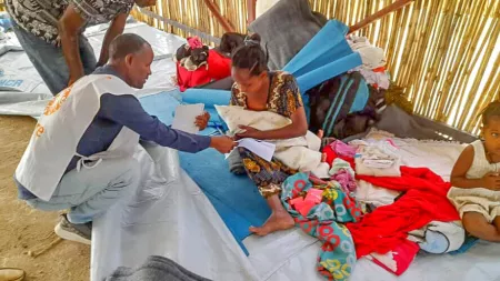 Woman sitting on the floor holding baby  and man handing out paper