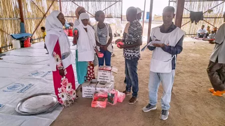 Three women and two men standing around boxes inside a tent