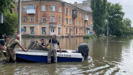 People carrying boat in flooded area with brown brick building in the background