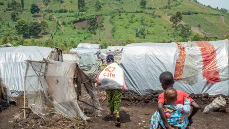 DRC_Woman carrying CARE package while child with another child on his back follows in refugee settlement