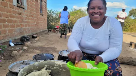 Zambia_Lady kneeling by three foot pots dishing up pap