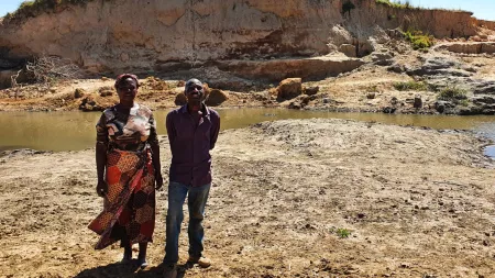 Zambia_Older couple standing in front of sand hill and drying dam